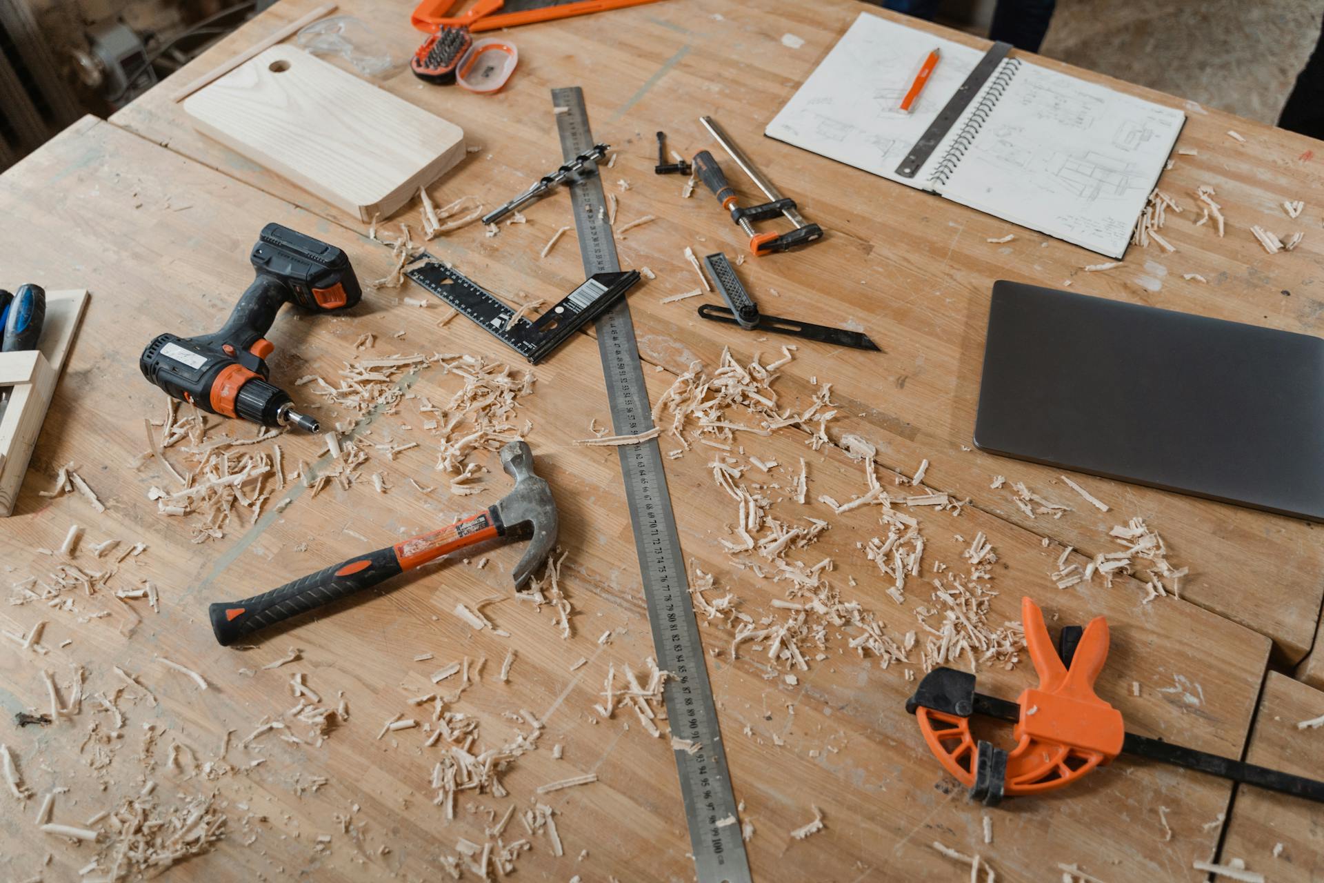 A workbench with various woodworking tools alongside sketches and wood shavings, indicating an active project.