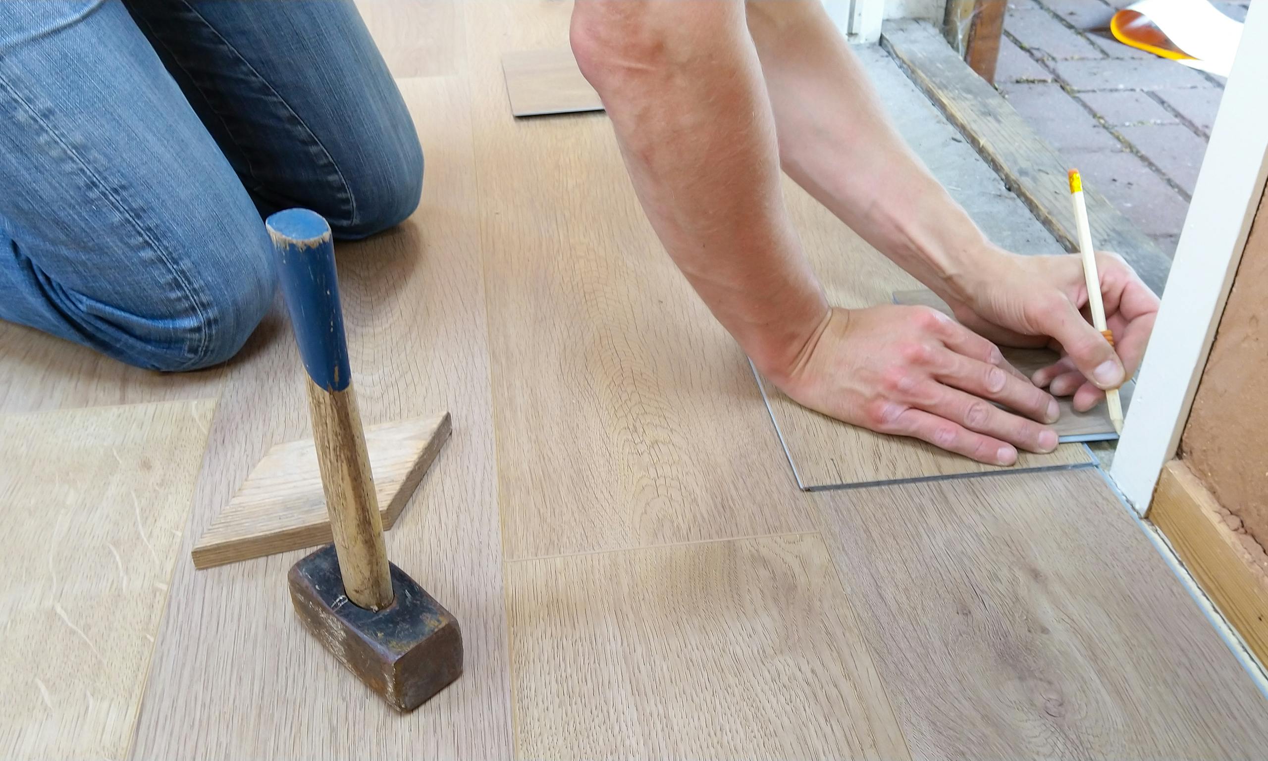 Carpet Fitting carefully measures and marks wooden floor panels for precise installation.
