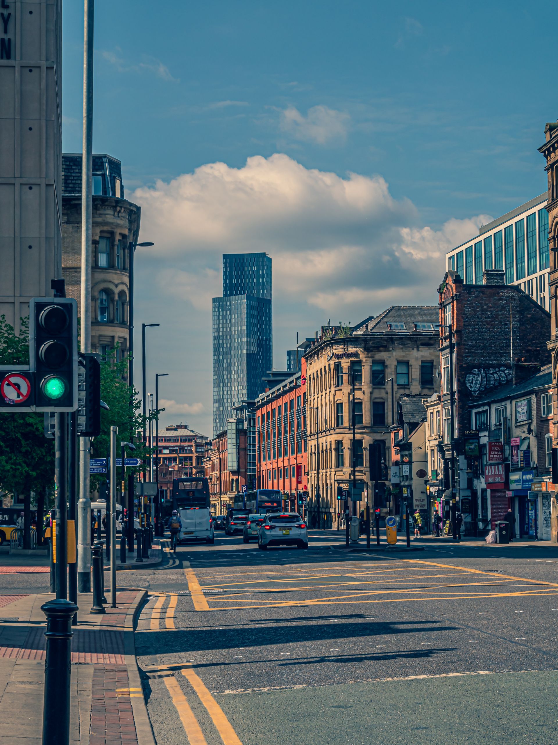 Dynamic urban scene in Manchester with historic and modern architecture under a sunny sky.